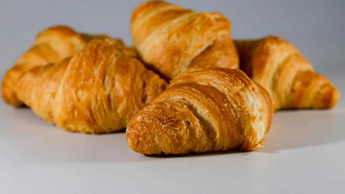 Croissant de mantequilla recién horneado junto a café con leche en mesa parisina